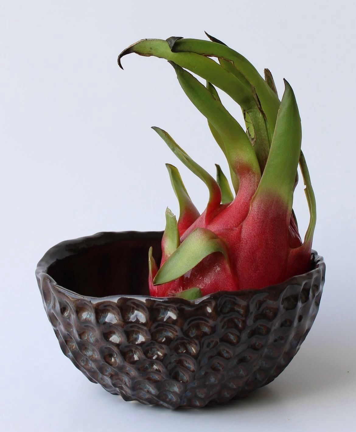 A dragon fruit held in a dark tactile ceramic bowl