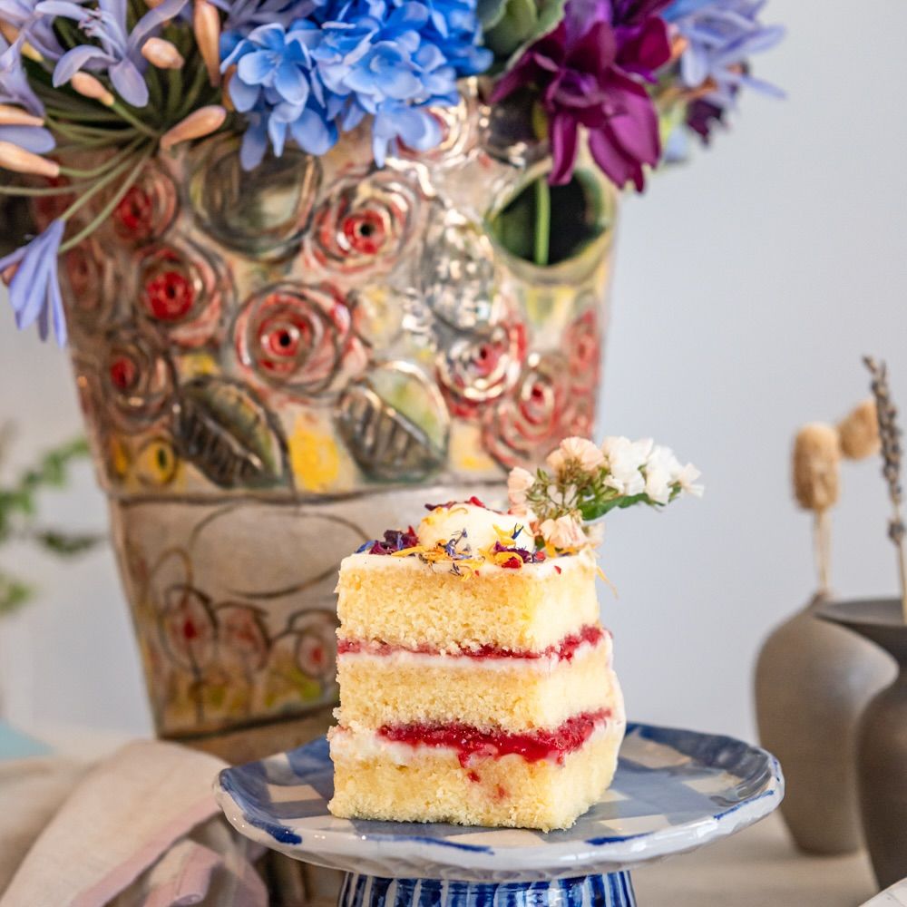 A flower-topped cake beside handmade ceramics on a sunlit table