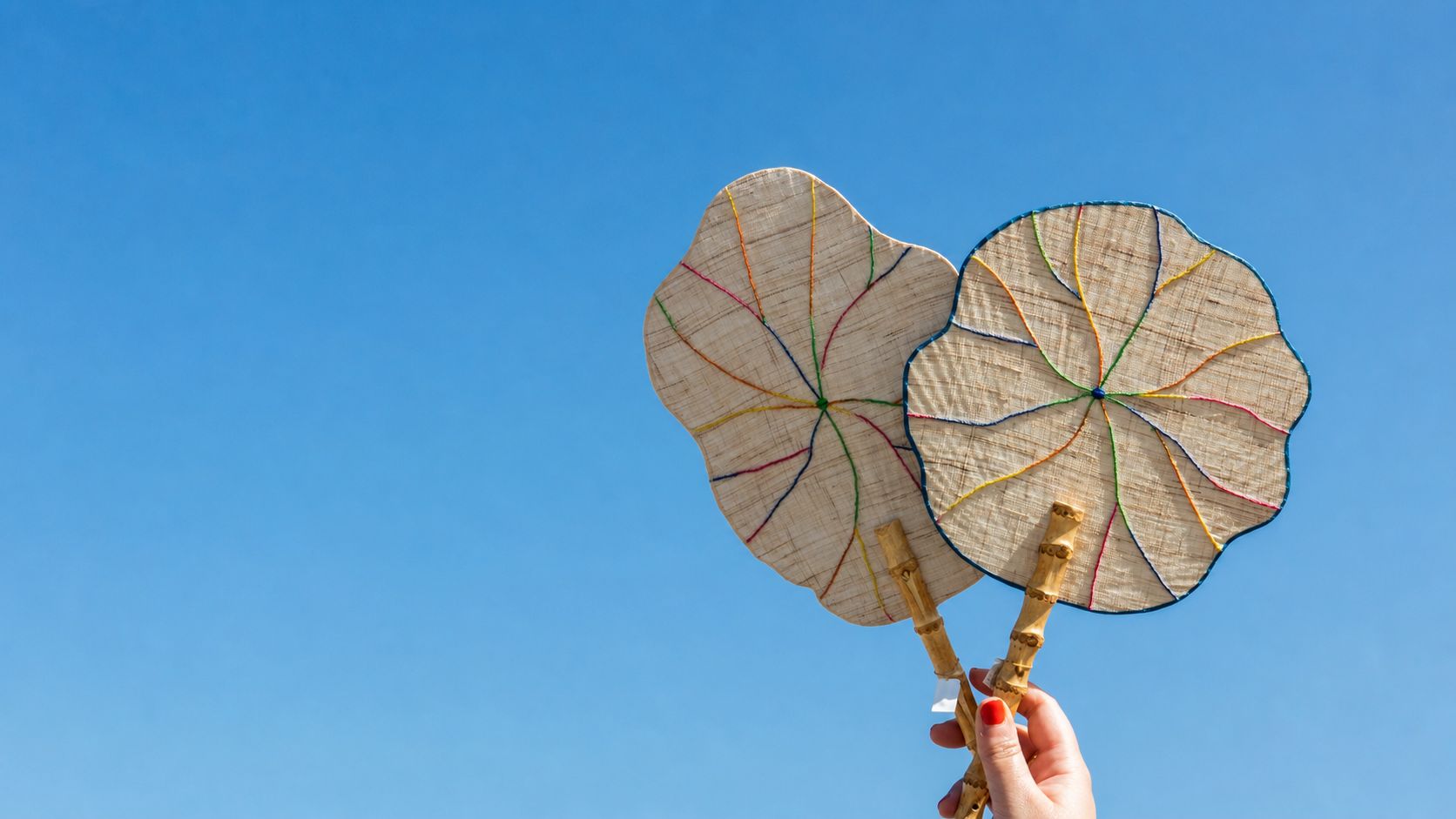 Two translucent handmade fans held against a brilliant blue sky