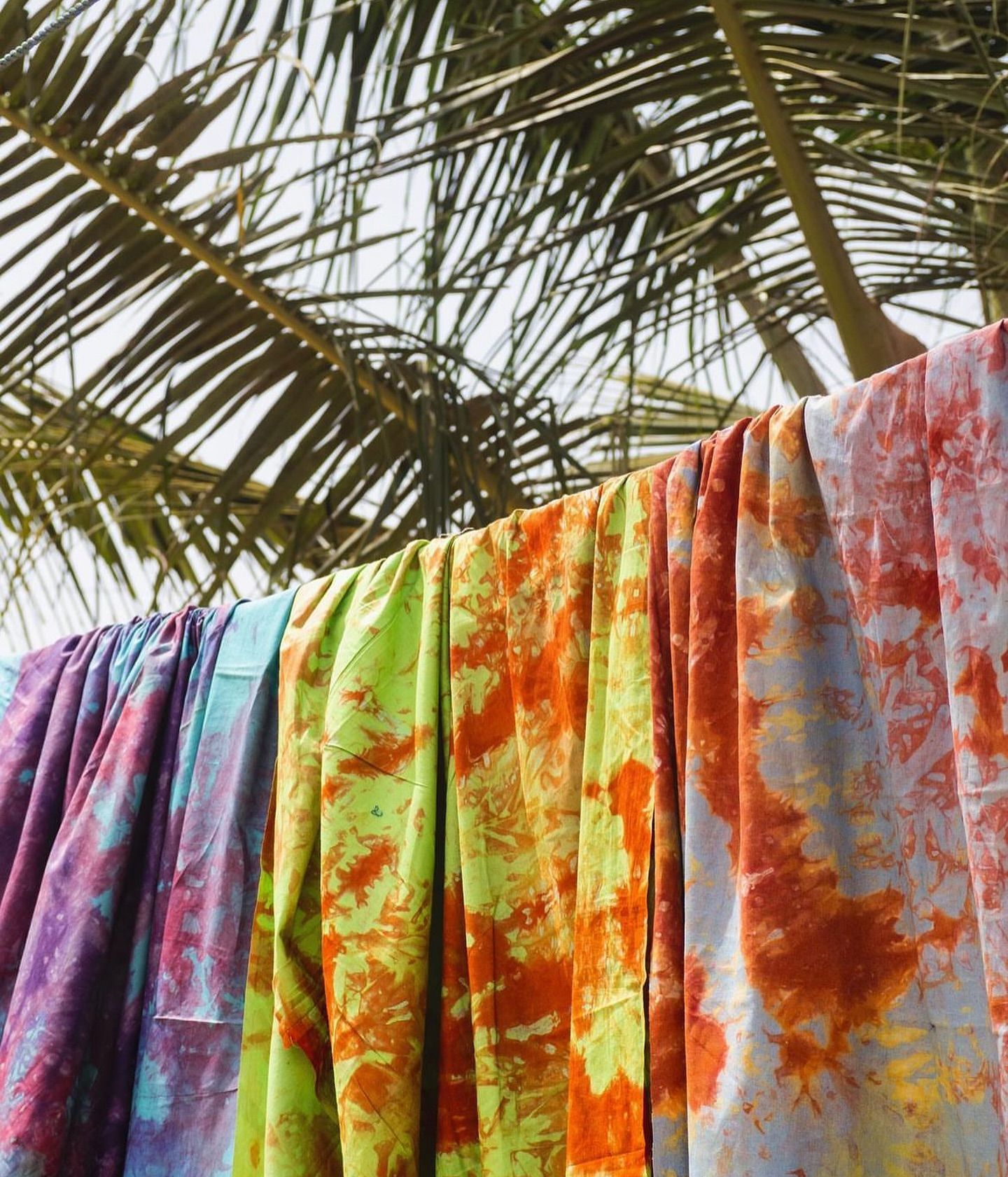 Hand-dyed textiles hanging beneath palm leaves